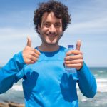 Smiling man enjoying a sunny day at the beach in Portugal, giving thumbs up.